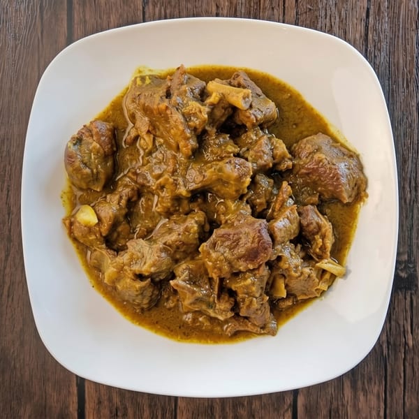 Close-up of a white plate filled with rich, brown curry and tender meat pieces on a wooden table.