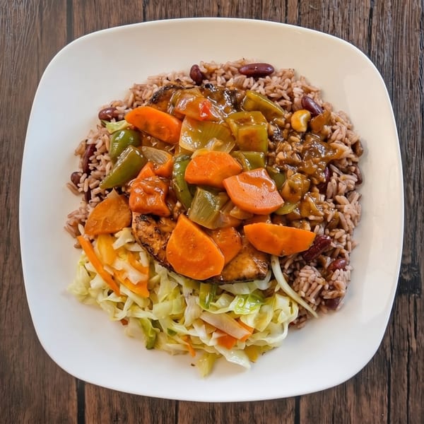 A plate of rice and peas with stewed chicken, carrots, bell peppers, and cabbage.