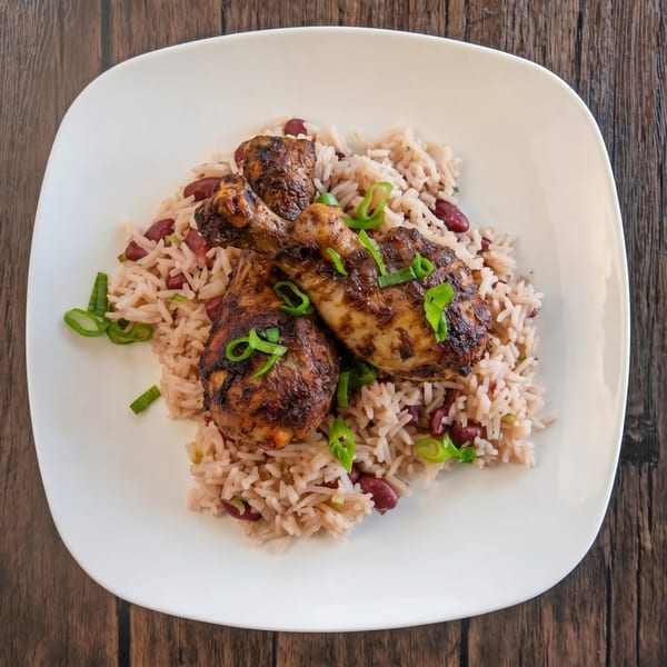 Three jerk chicken drumsticks on a bed of rice and peas, garnished with green onions.