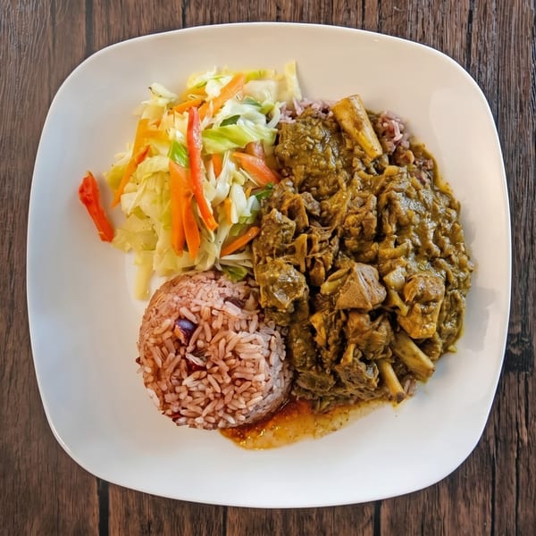 Curried goat with rice and peas, and steamed cabbage on a white plate.